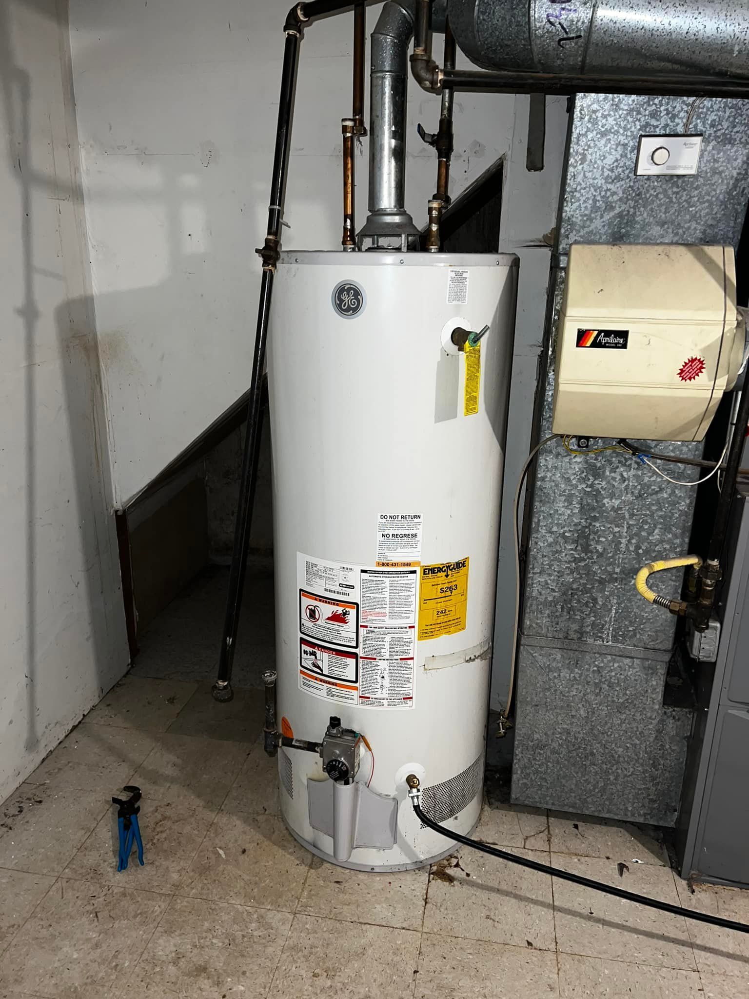 A water heater and furnace in a basement. The water heater is white, and the furnace is metallic gray.