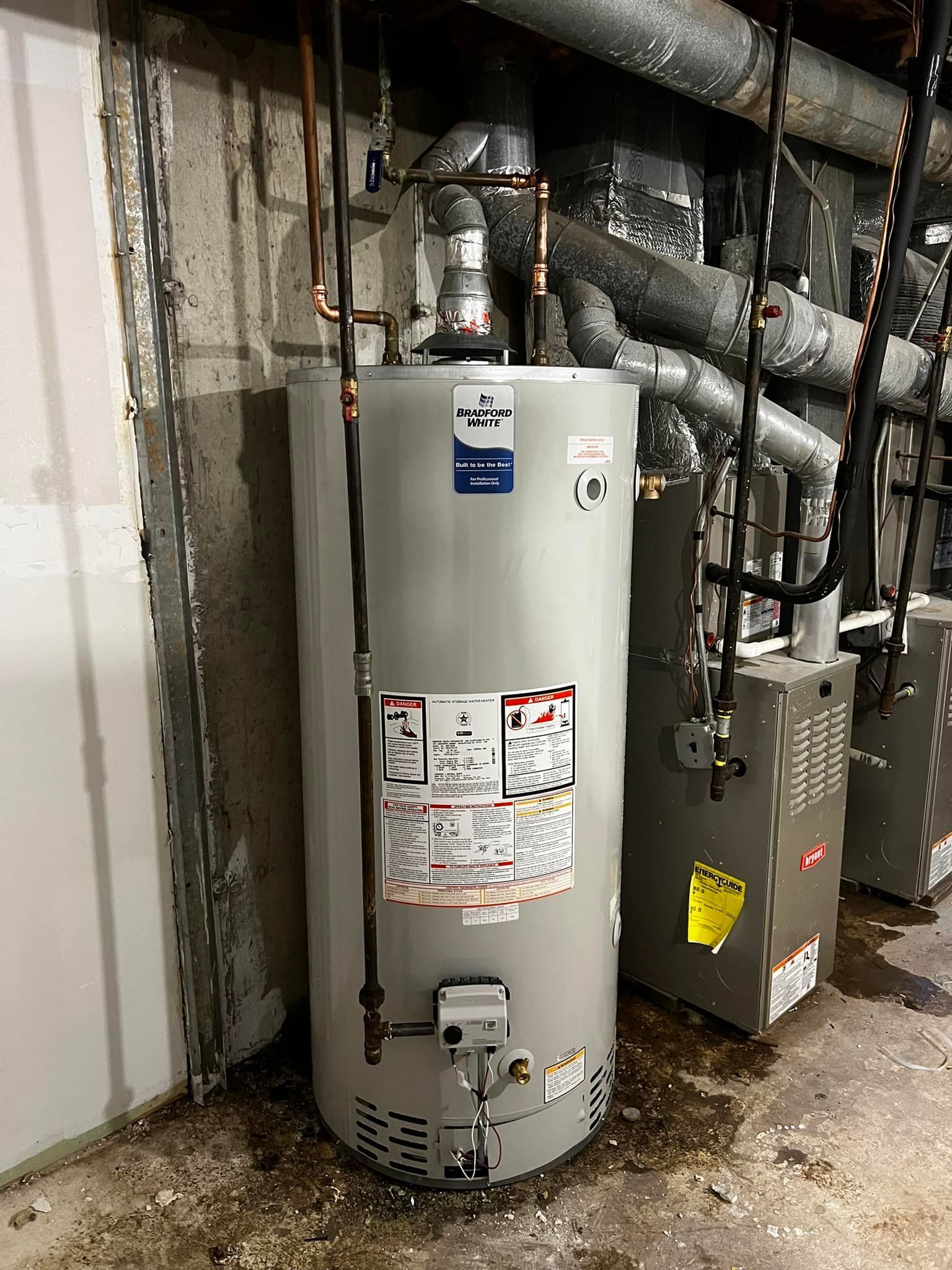Tall, gray water heater in a utility room, with copper pipes and HVAC units.