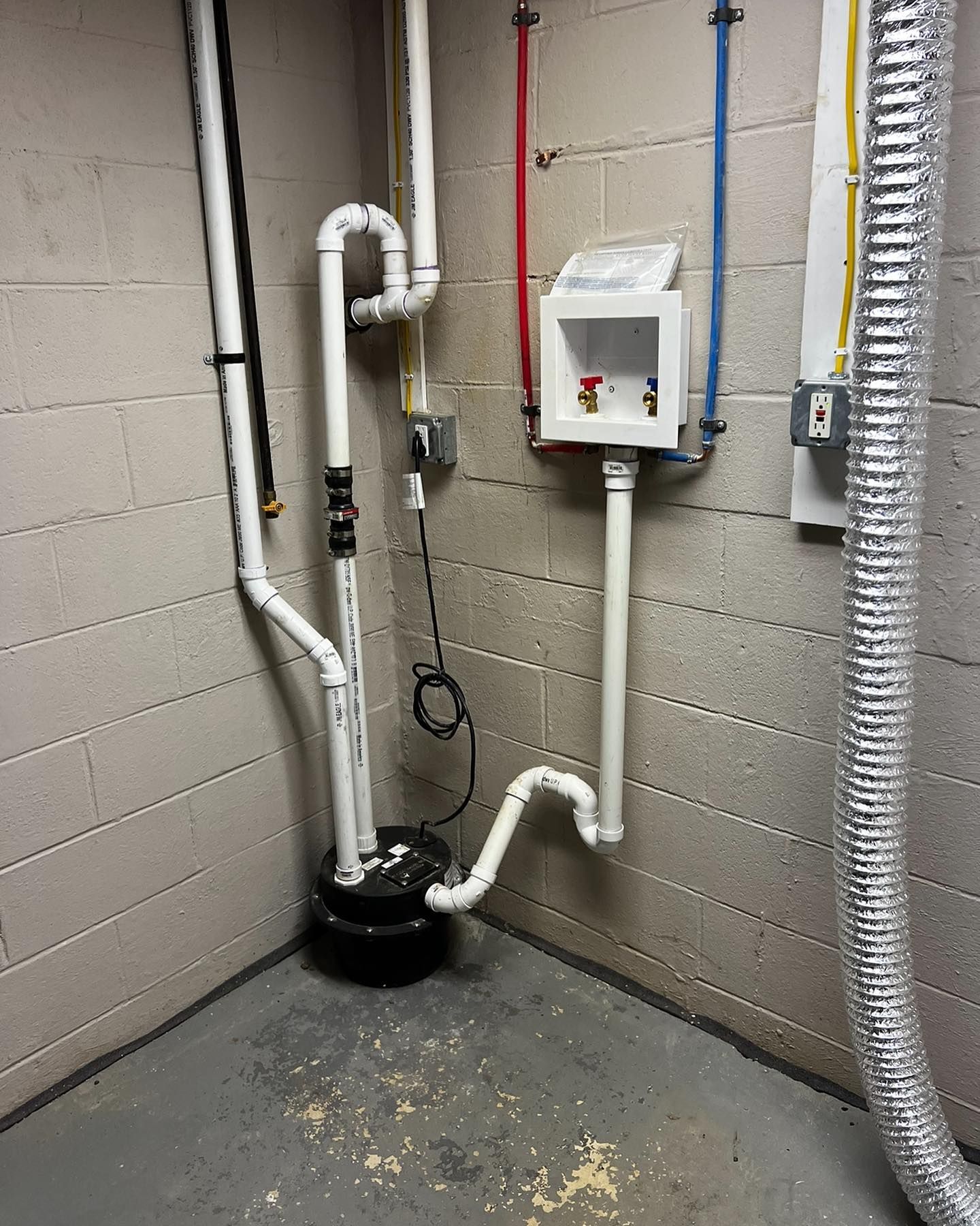 White plumbing pipes against a gray cinder block wall. A sump pump and washing machine hookups are visible.