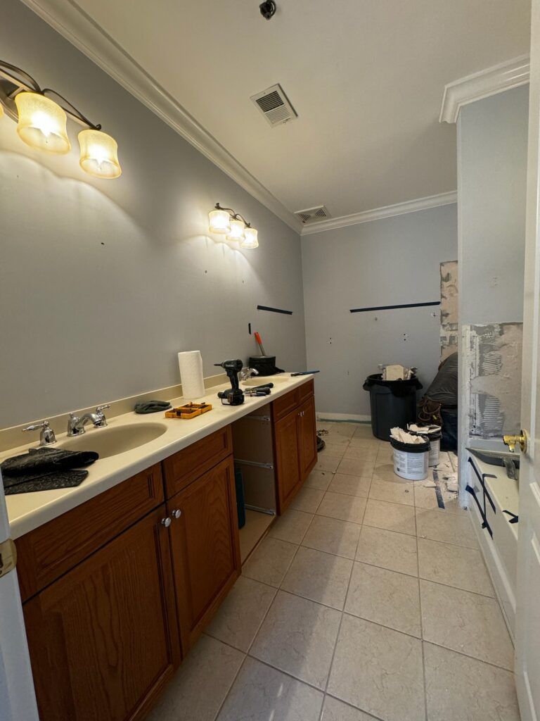 Bathroom renovation with double vanity, blue-gray walls, tile floor, and debris.