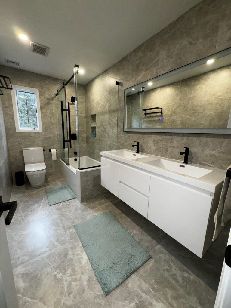 Modern bathroom with gray tile walls, white vanity, black fixtures, and a shower with a glass door.