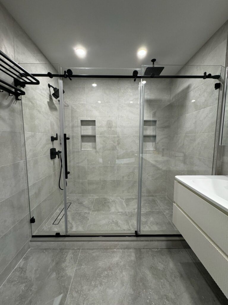 Modern bathroom with gray tiled walls, black framed glass shower, and floating vanity.