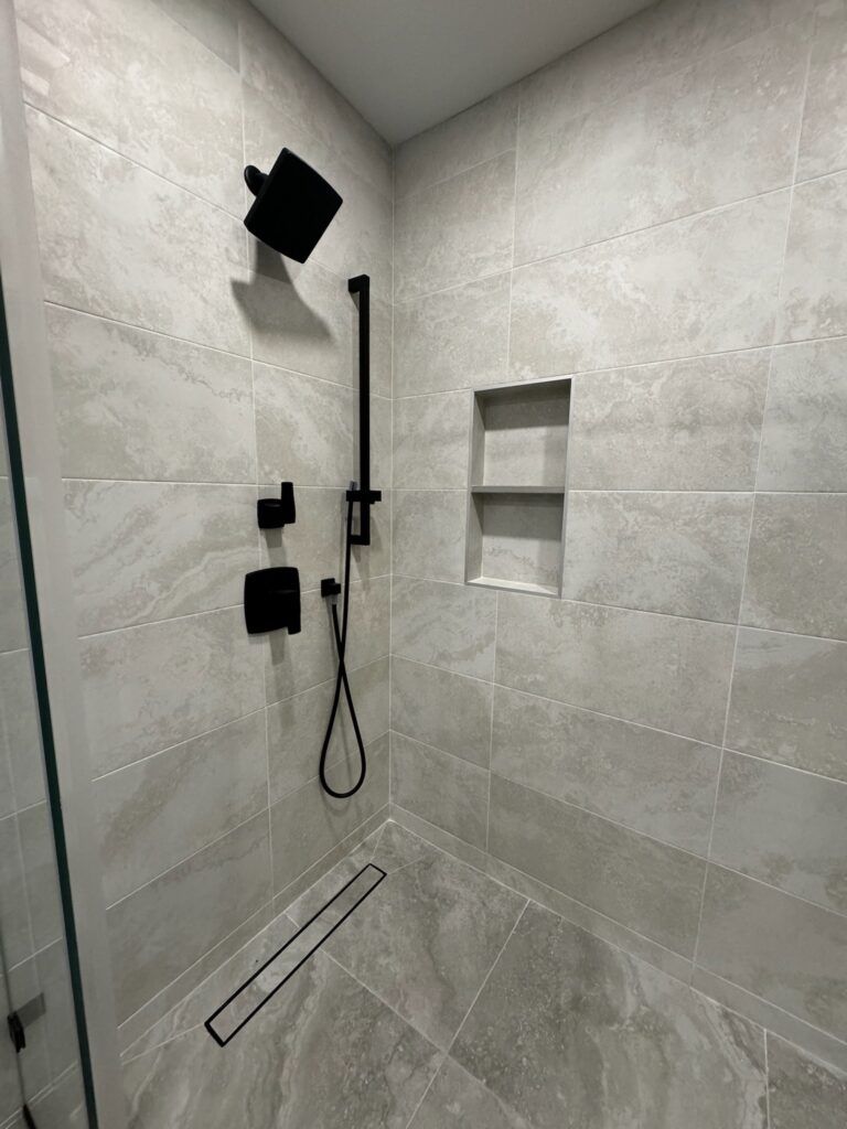 Modern shower with black fixtures, grey tile, and a built-in shelf.