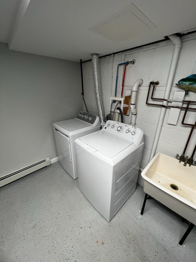 Laundry room with a washing machine, dryer, utility sink, and pipes against a gray and white wall.