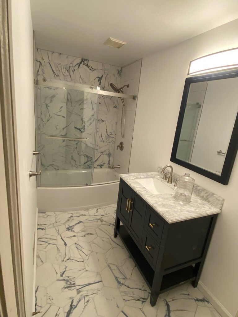 Bathroom with marble-patterned tile, black vanity, and shower. White walls, chrome fixtures.