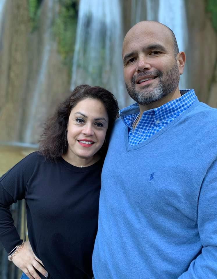 A man and a woman are posing for a picture together . the man is wearing a blue sweater.