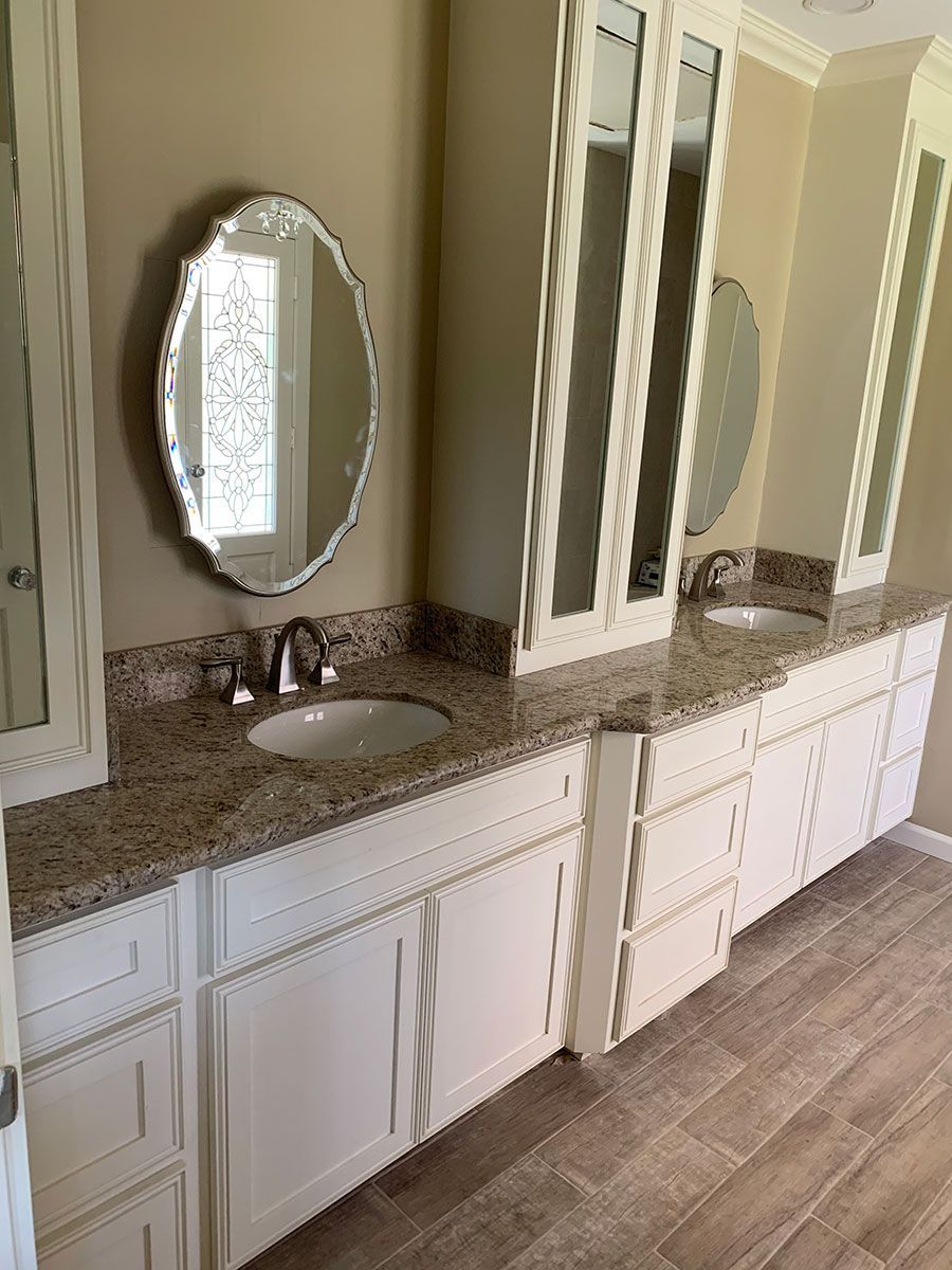 A bathroom with two sinks , a mirror , and white cabinets.