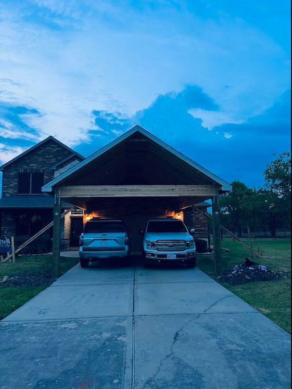 Two cars are parked under a carport in front of a house.