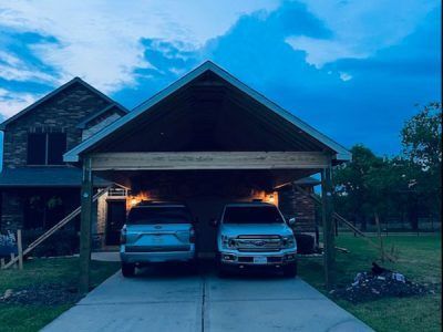 Two cars are parked under a carport in front of a house.