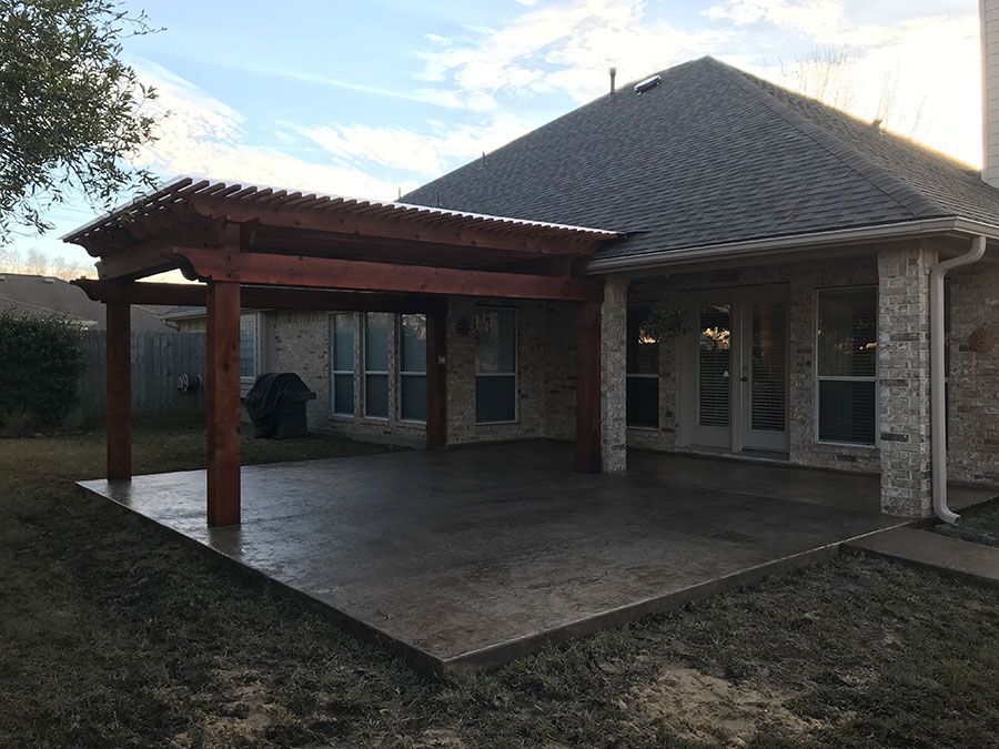 A wooden pergola is sitting on top of a concrete patio in front of a house.