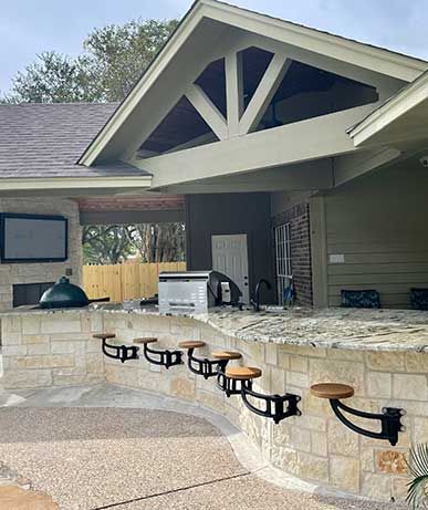 A large brick outdoor kitchen with stools and a grill.