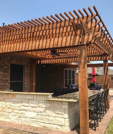 A wooden pergola over a brick building with a bar and chairs underneath it.