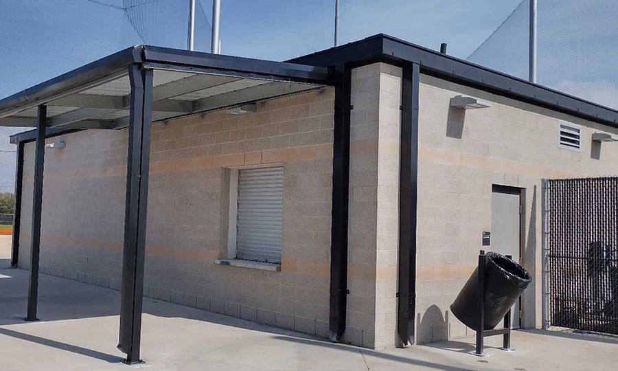 A brick building with a black roof and a trash can in front of it.