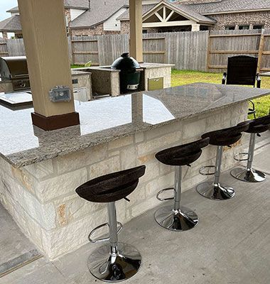 A patio with a bar and stools and a grill.