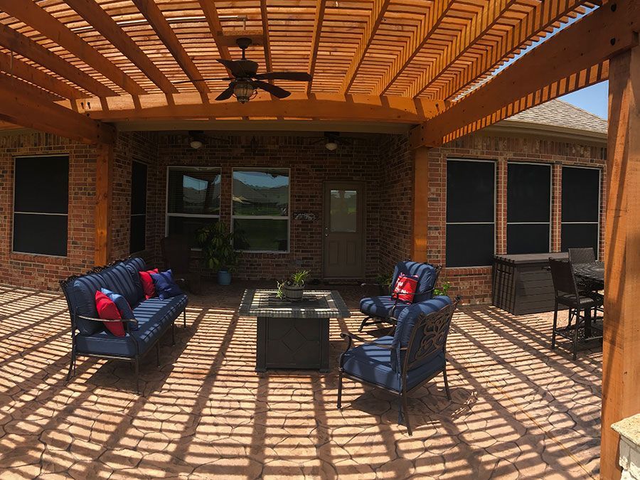 A patio with a couch , chairs , and a table under a pergola with a ceiling fan.