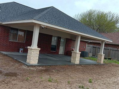 A brick house with a covered porch and a concrete patio in front of it.