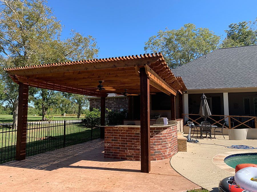 A wooden pergola over a brick bar in front of a house.