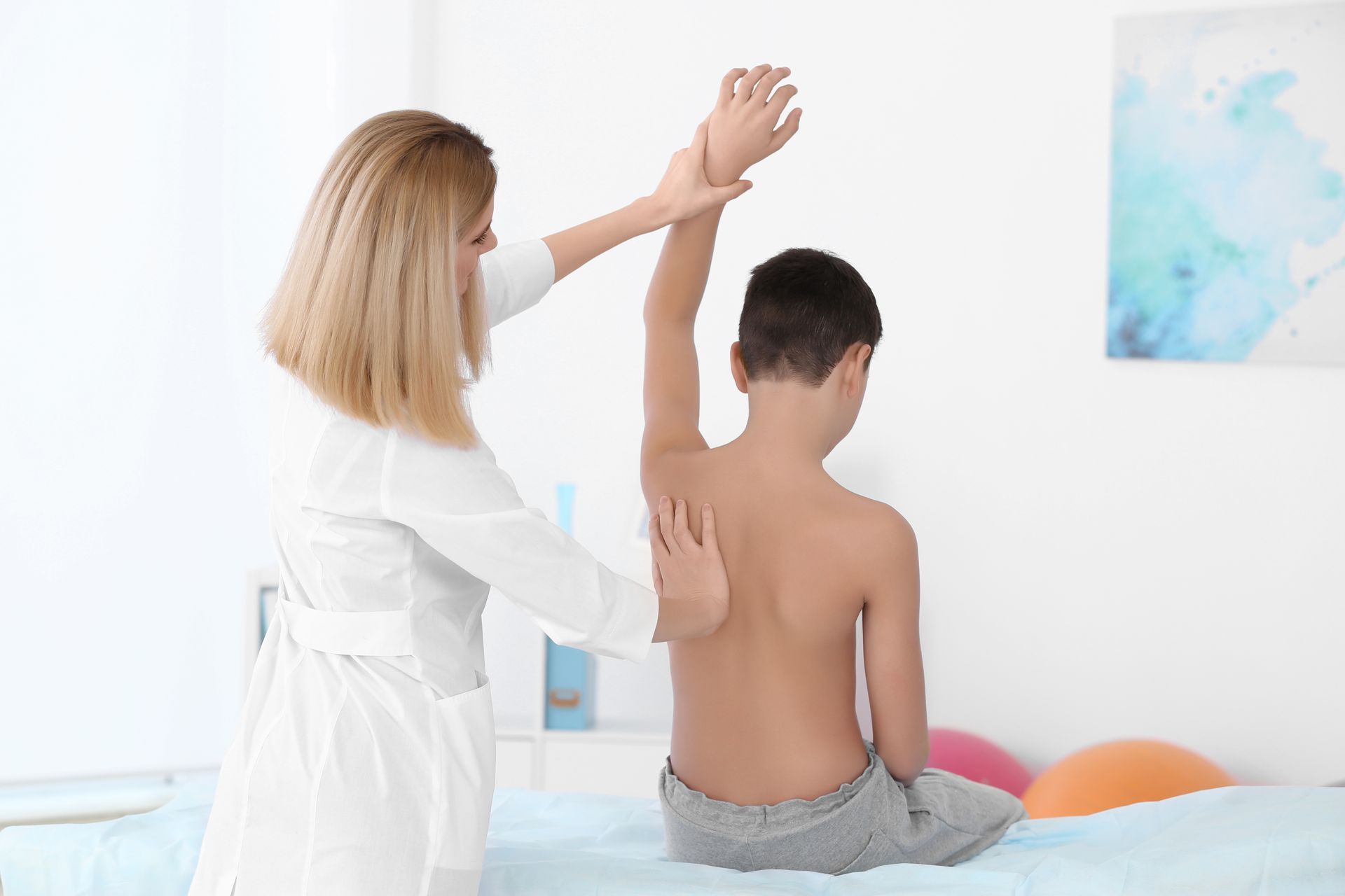 A healthcare provider examines a boy's shoulder in a clinic.