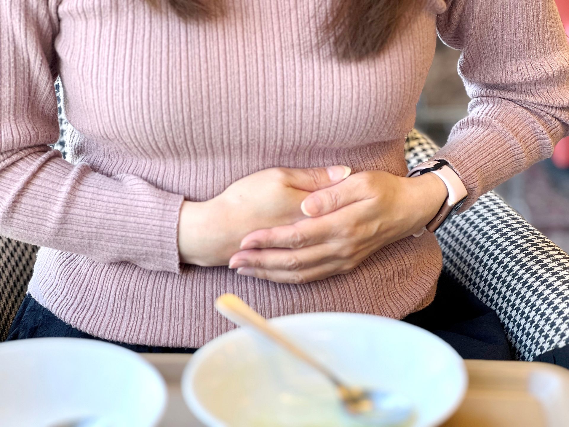 A woman is sitting at a table with her hands on her stomach.