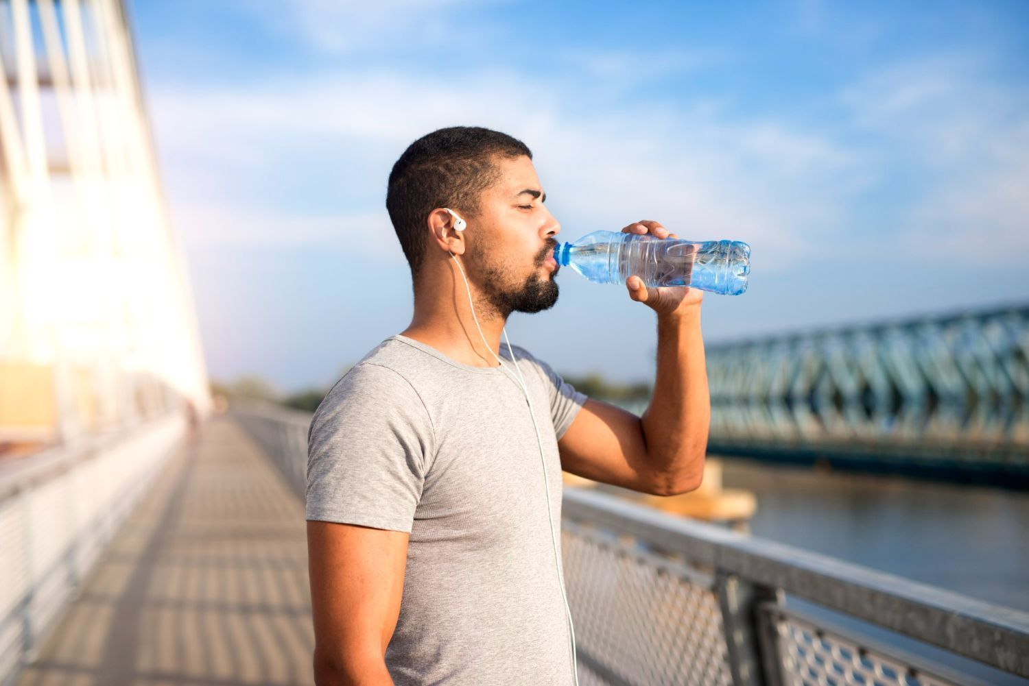 A man is drinking water from a bottle on a bridge.