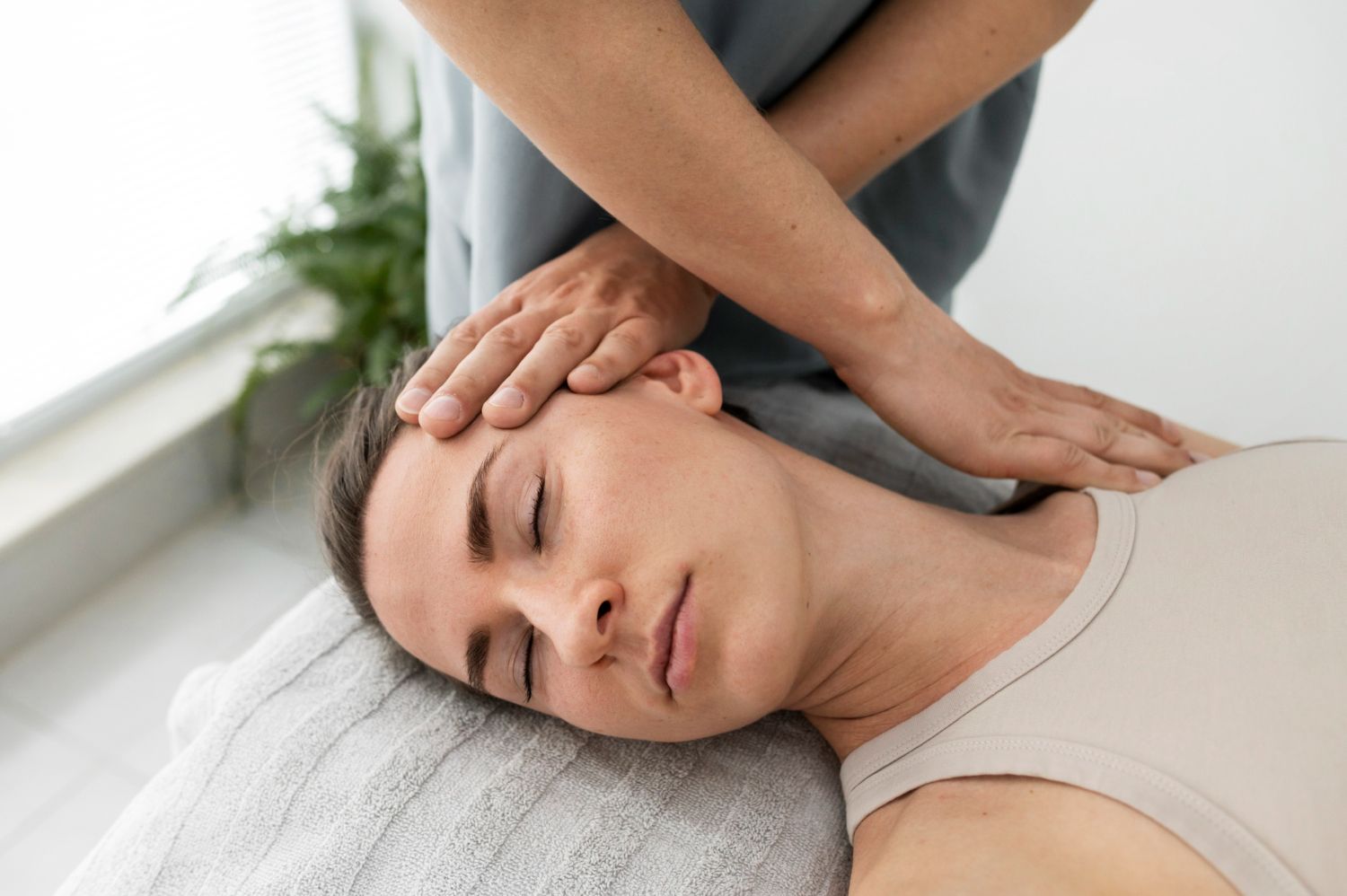Person receiving neck massage; hands on head and shoulders, eyes closed, indoors.
