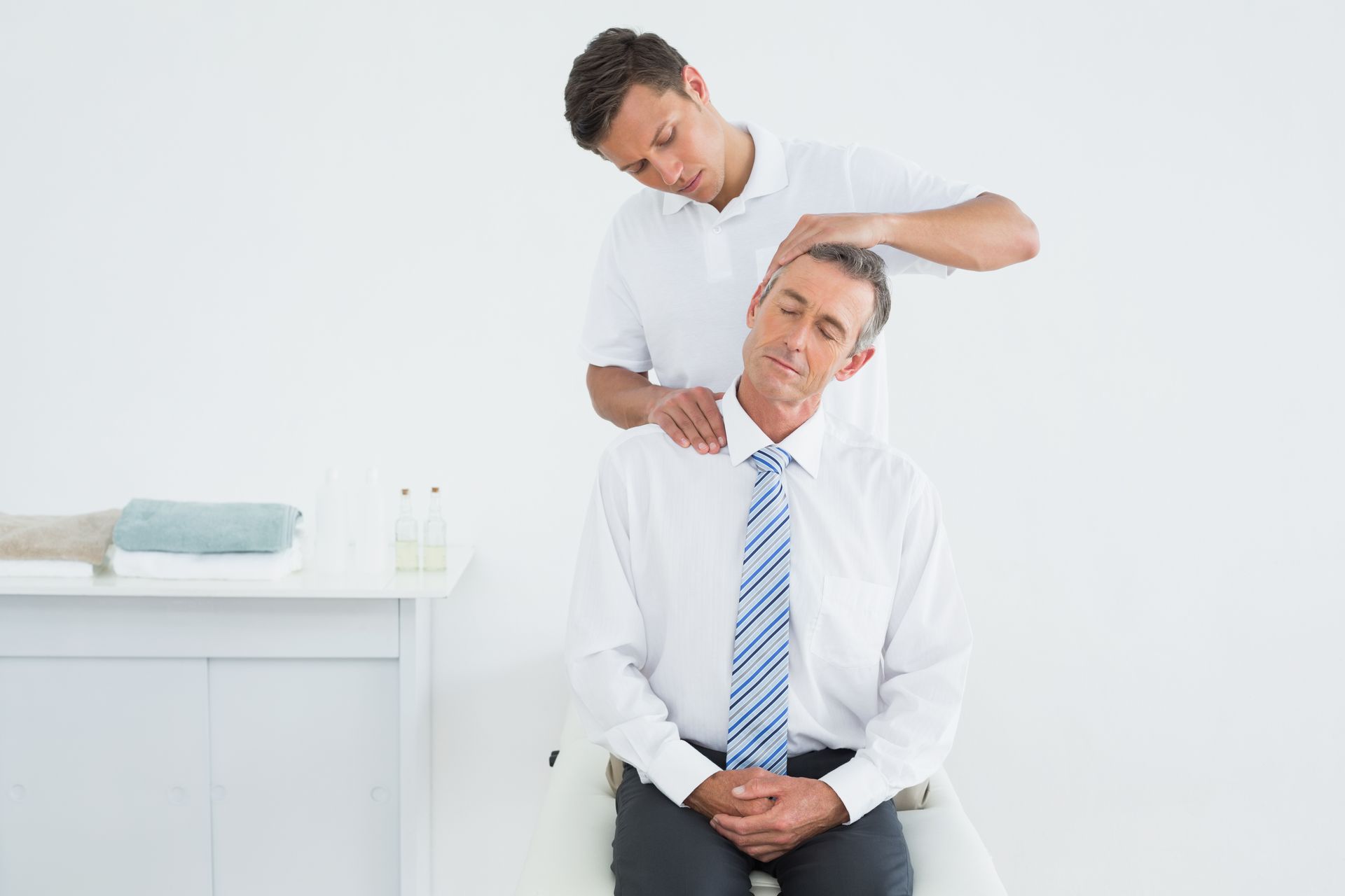 Man receiving neck massage from a therapist in a white room.