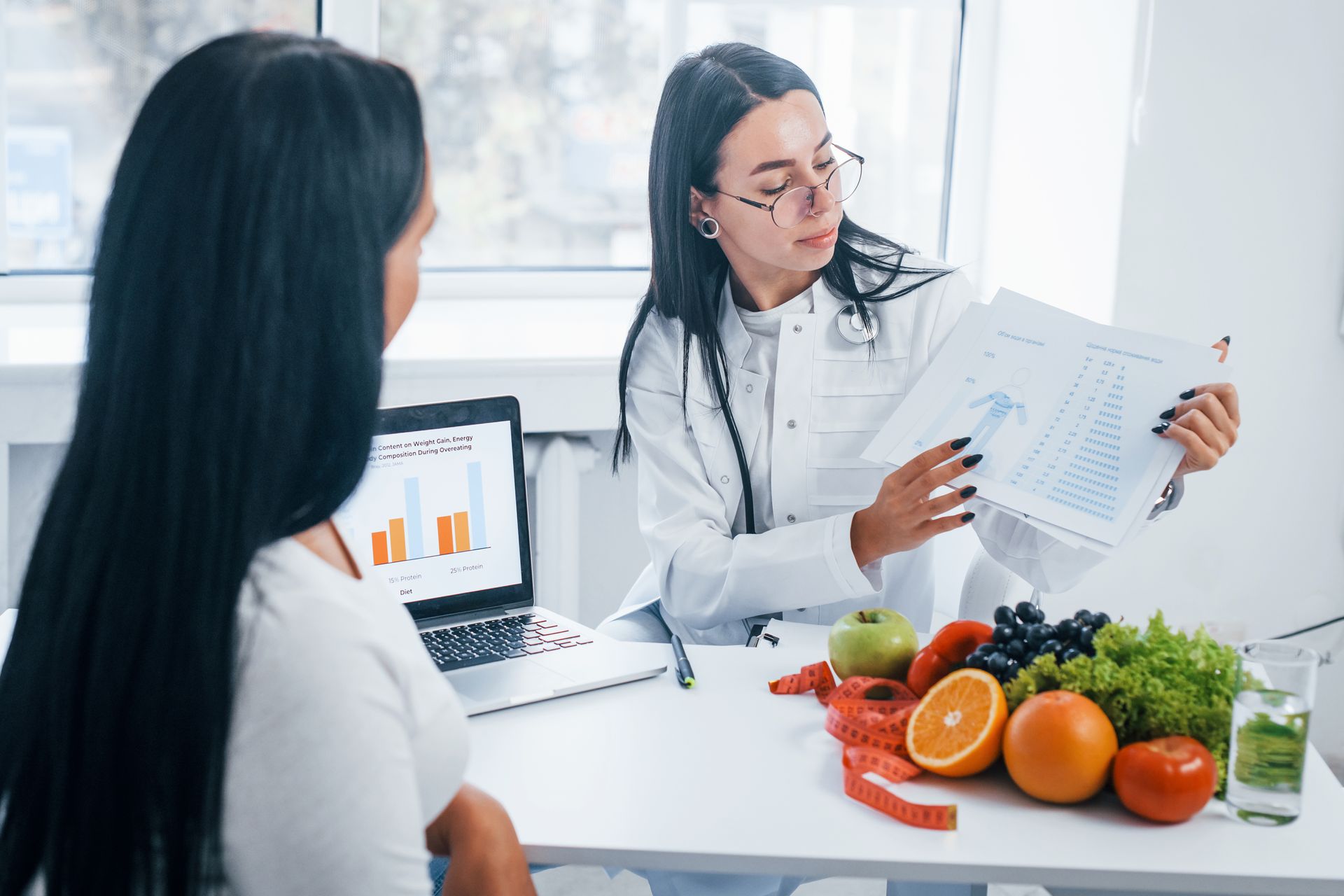 A woman is sitting at a table with fruits and vegetables and talking to a doctor.