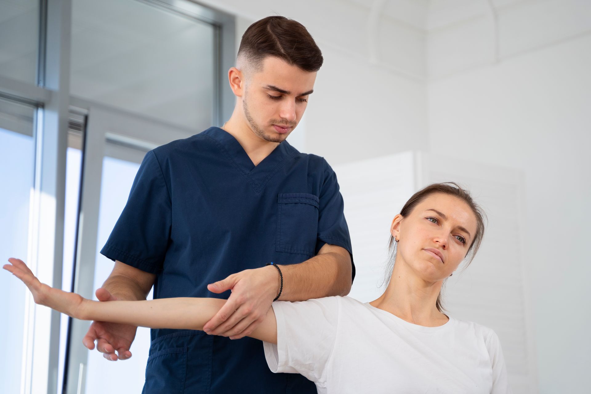 A man is helping a woman stretch her arm in a hospital.