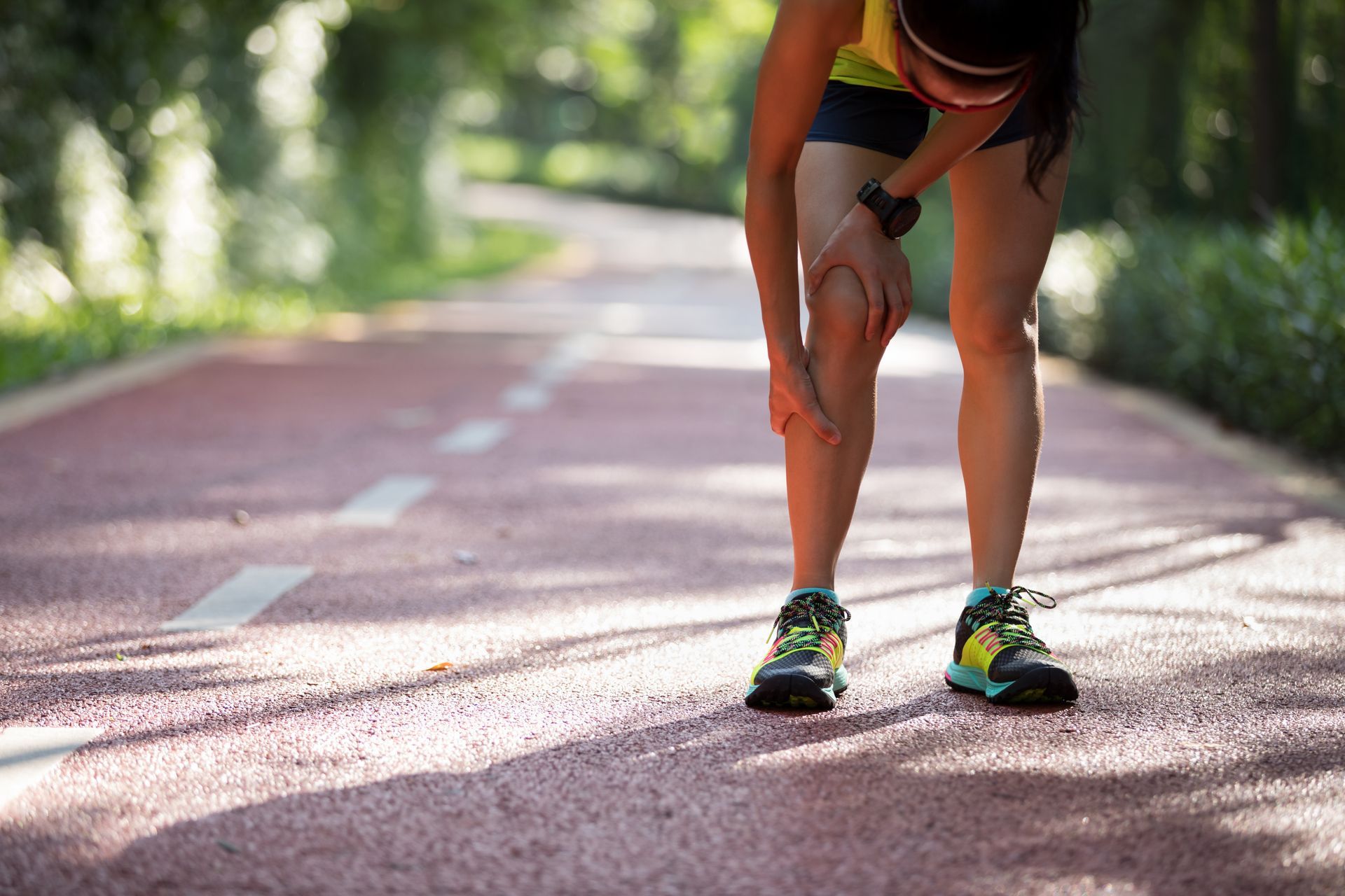 Runner clutching leg in pain on a red track.