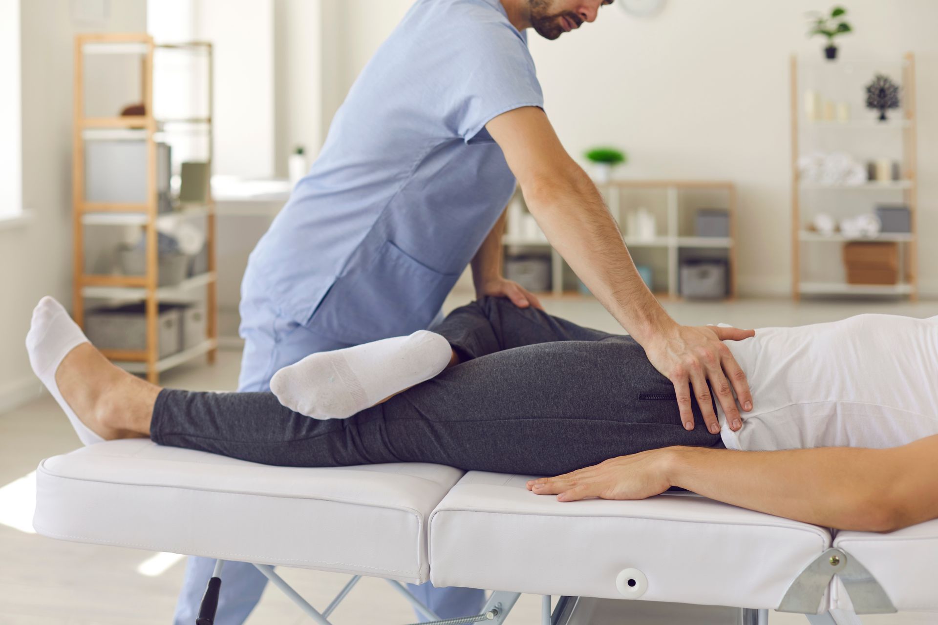 Physical therapist working on a patient's leg and hip on an examination table.