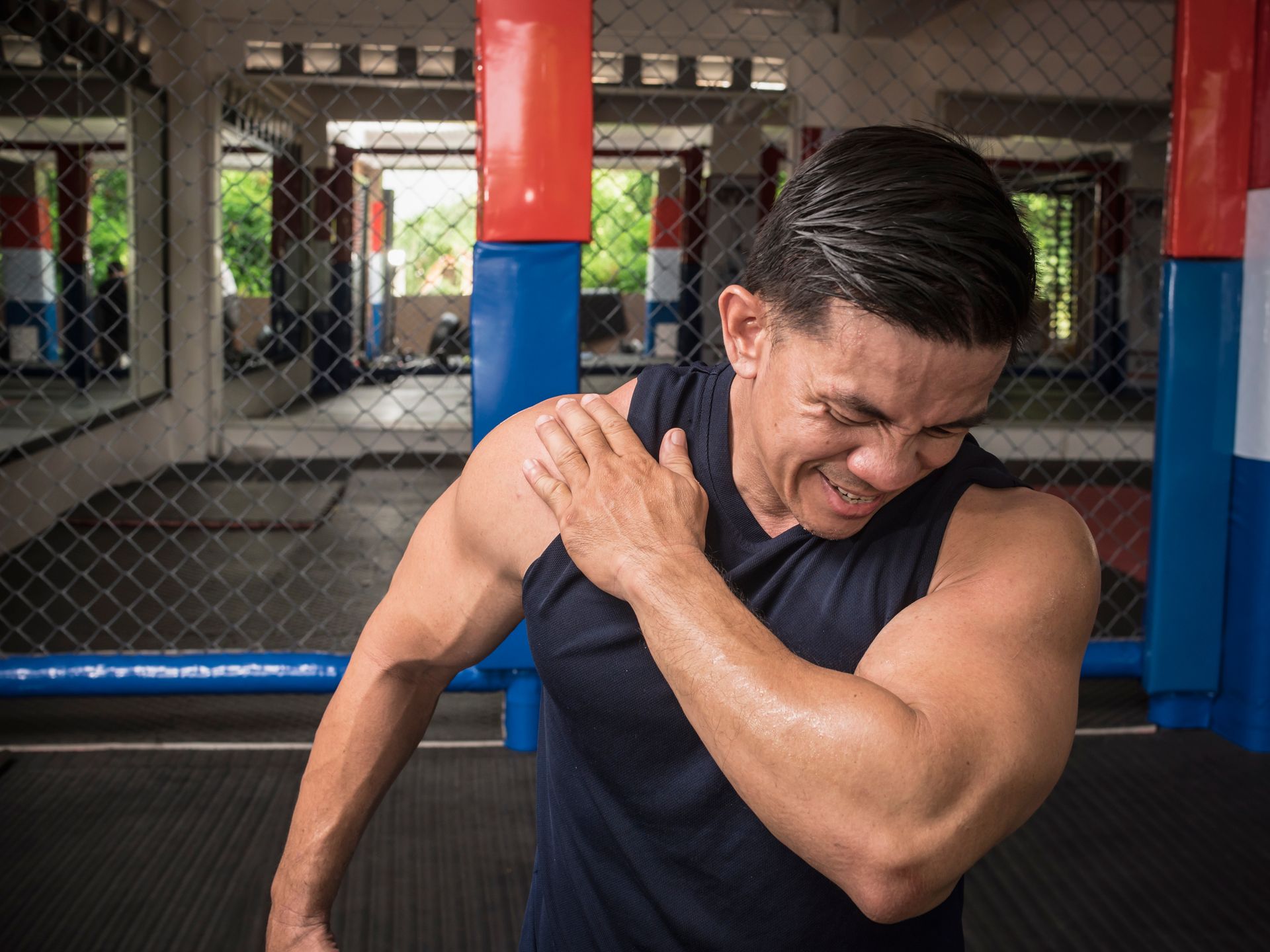 Man with shoulder pain at a gym, grasping his shoulder, grimacing.