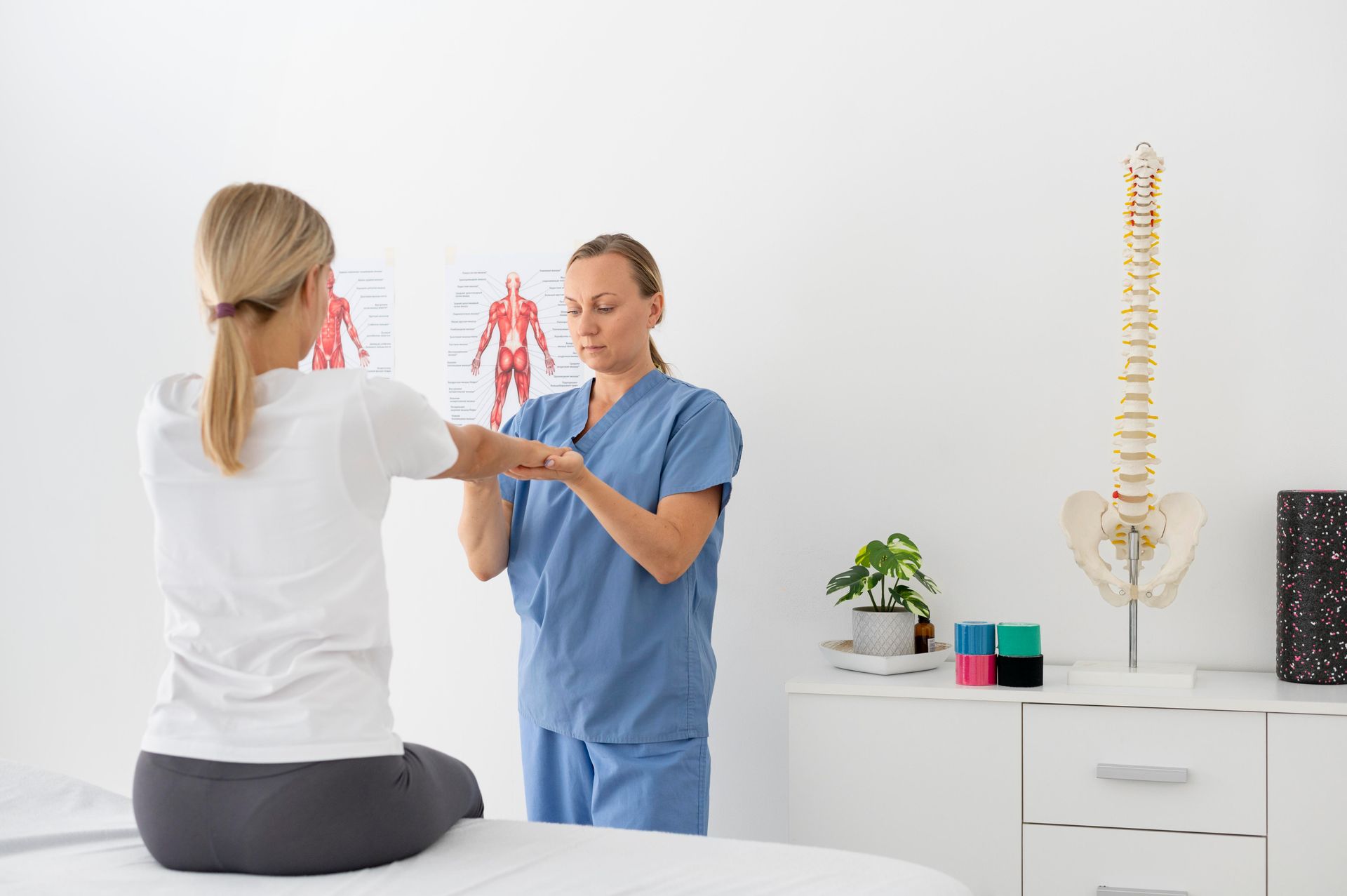 A woman is sitting on a bed while a nurse examines her back.