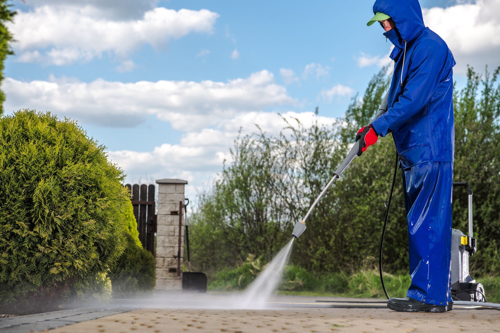 Person in blue coveralls pressure washing a driveway on a sunny day.