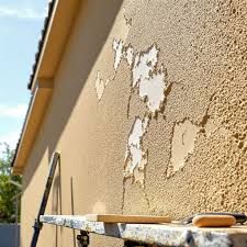 Person painting horizontal siding with a brush; wearing work gloves and a light gray shirt. Person painting horizontal siding with a brush; wearing work gloves and a light gray shirt.