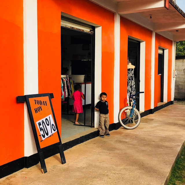 Specialty Leasing - Ancillary Income for Parking Lots Shopping Centers Orange storefront with sale sign, two children at the entrance, and a bicycle leaning nearby
