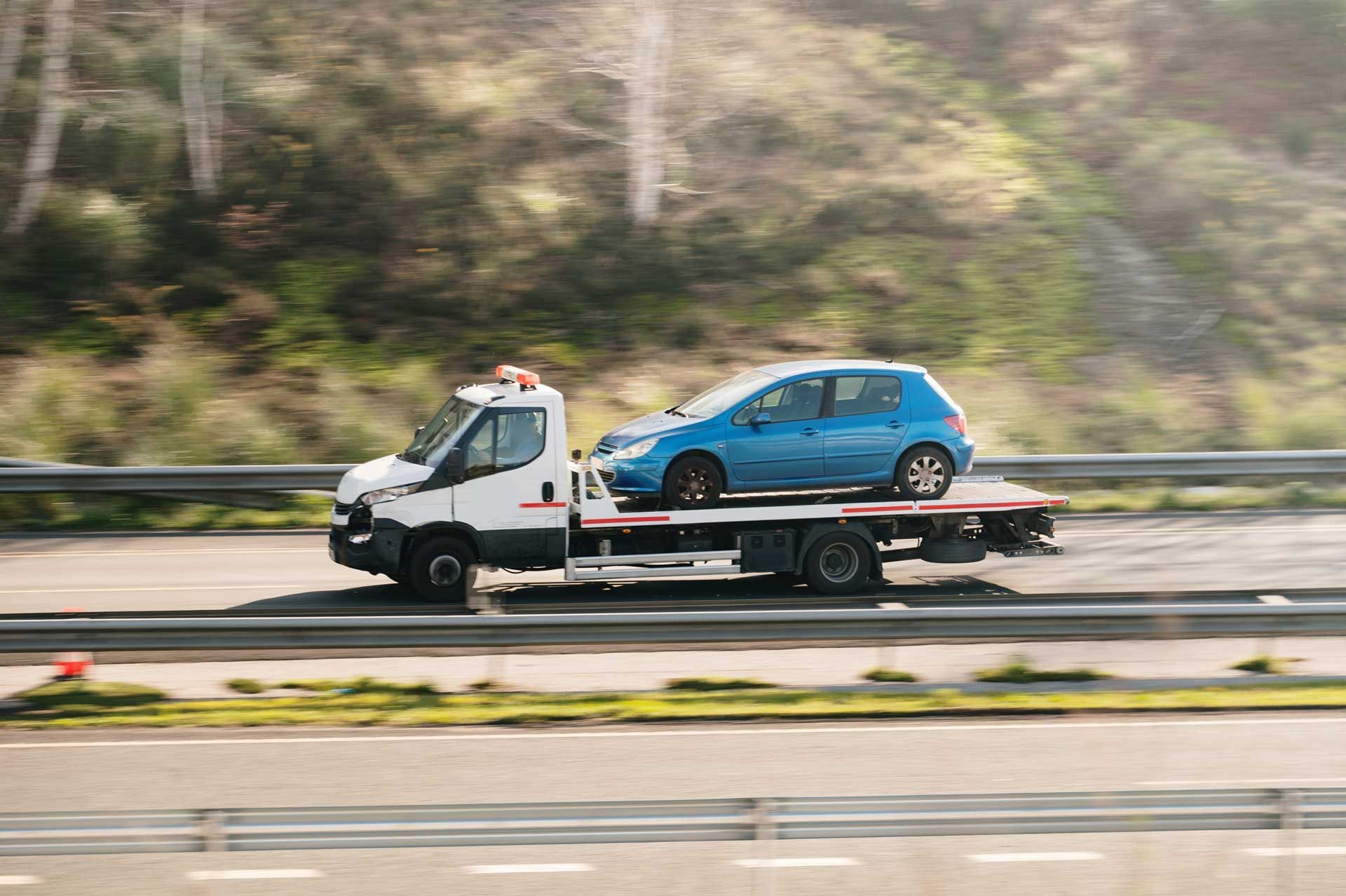 A tow truck is transporting a blue car on a highway.
