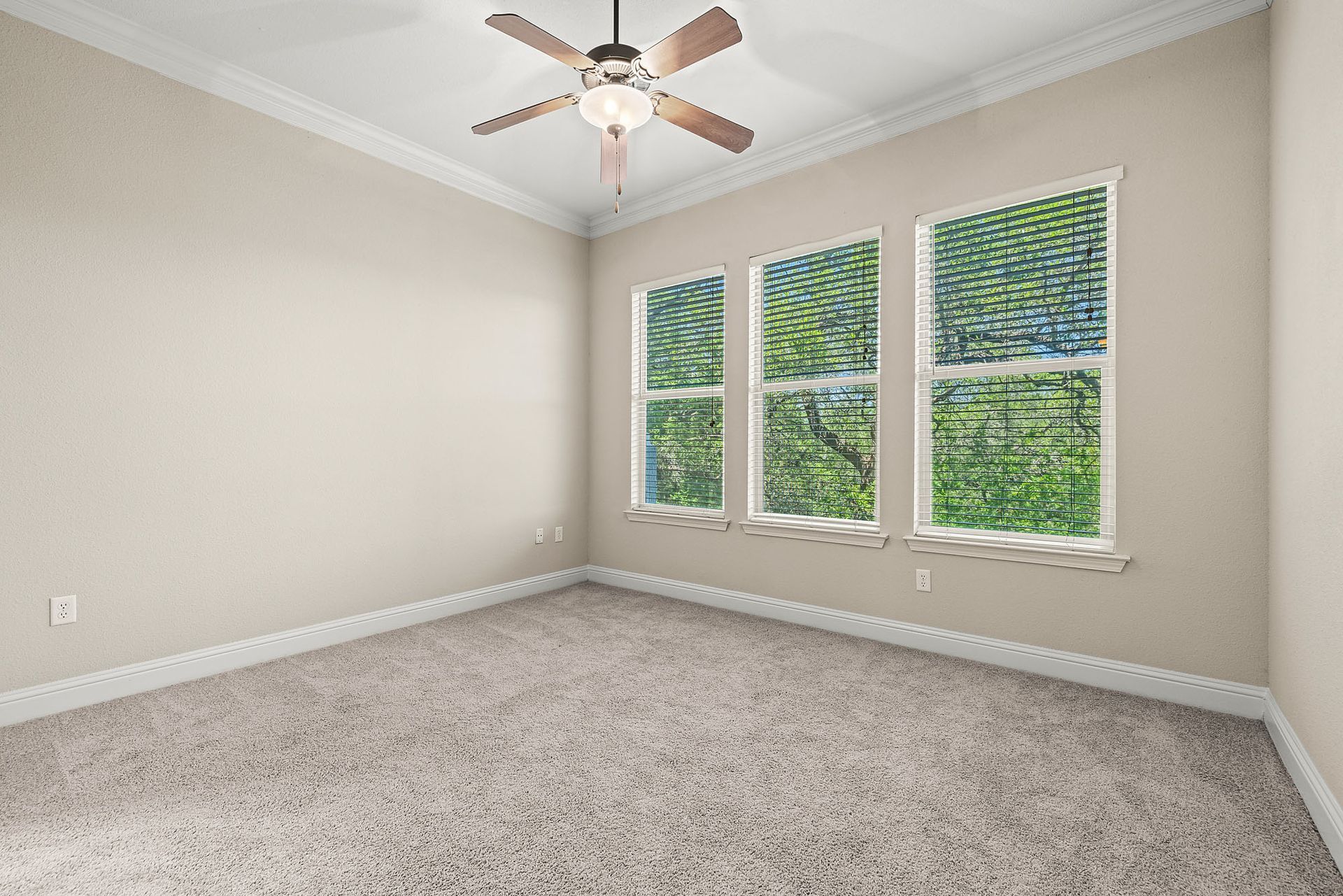 Empty room with beige walls, carpet, and three windows overlooking greenery at Marquis at TPC, offers pet-friendly apartments in San Antonio, TX.