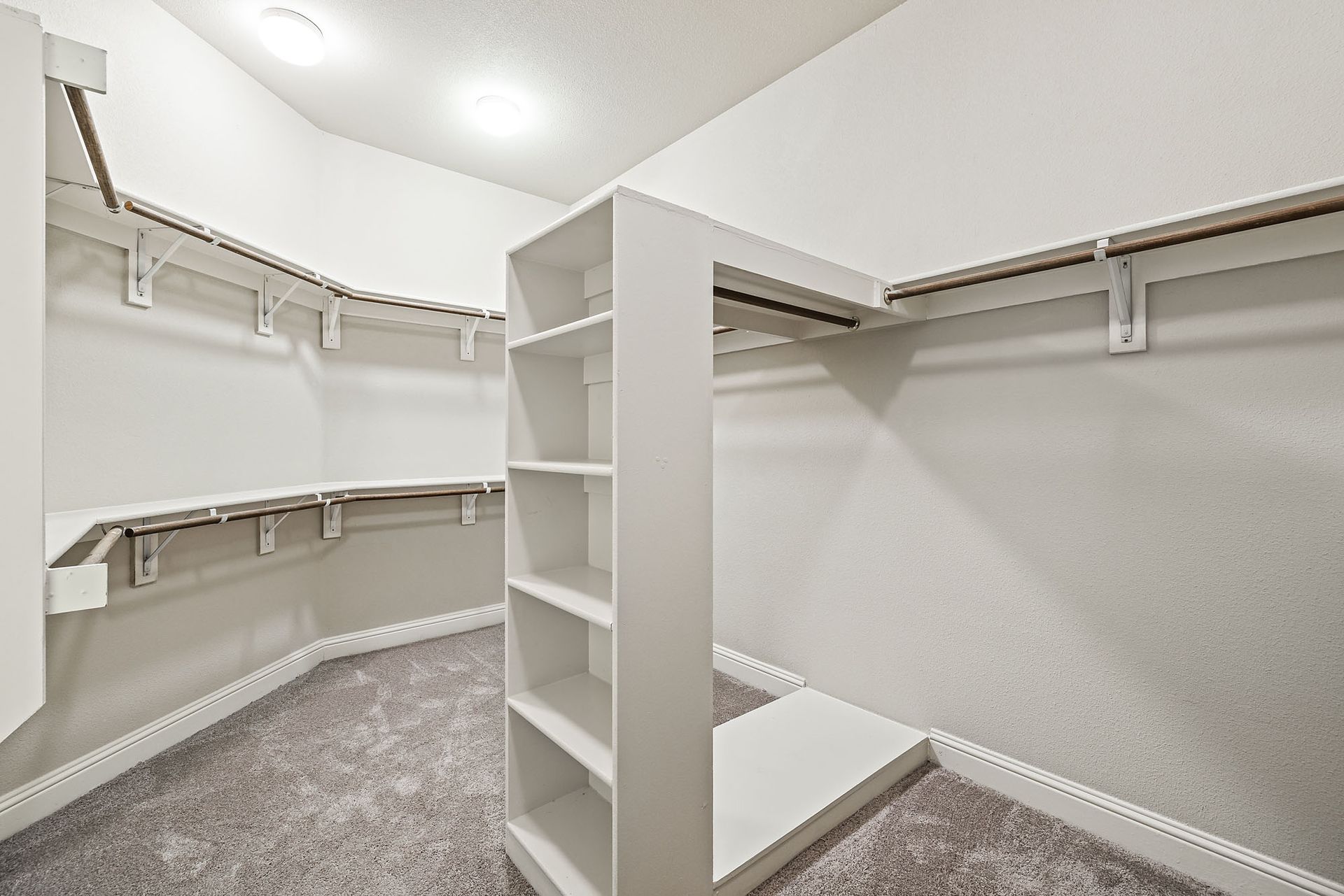 A walk-in closet with white shelving and a central shelving unit at Marquis at TPC, offers apartments for rent in San Antonio, TX. The floor is covered with gray carpeting 