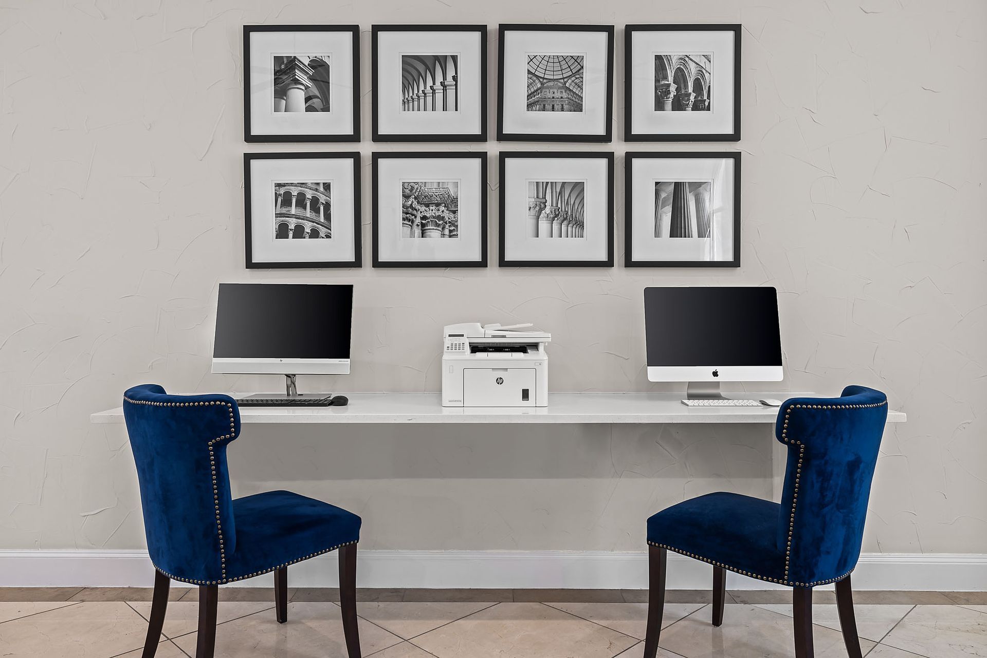 A business center with two computers, a printer, two blue chairs, and framed black and white photos on the wall at Marquis at TPC, offers townhomes for rent in San Antonio, TX.