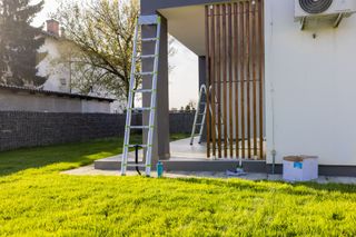 A ladder is sitting in the grass in front of a house. A ladder is sitting in the grass in front of a house.