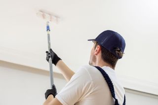 A man is painting the ceiling with a paint roller. A man is painting the ceiling with a paint roller.