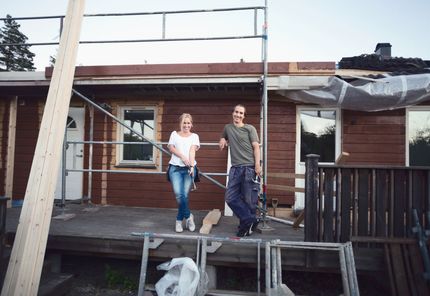 A man and a woman are standing on a deck in front of a house under construction. A man and a woman are standing on a deck in front of a house under construction.