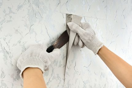 A person is removing wallpaper from a wall with a spatula. A person is removing wallpaper from a wall with a spatula.