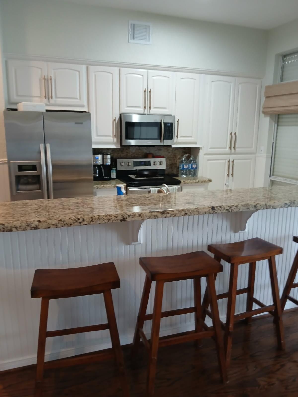A kitchen with stools and a refrigerator and microwave