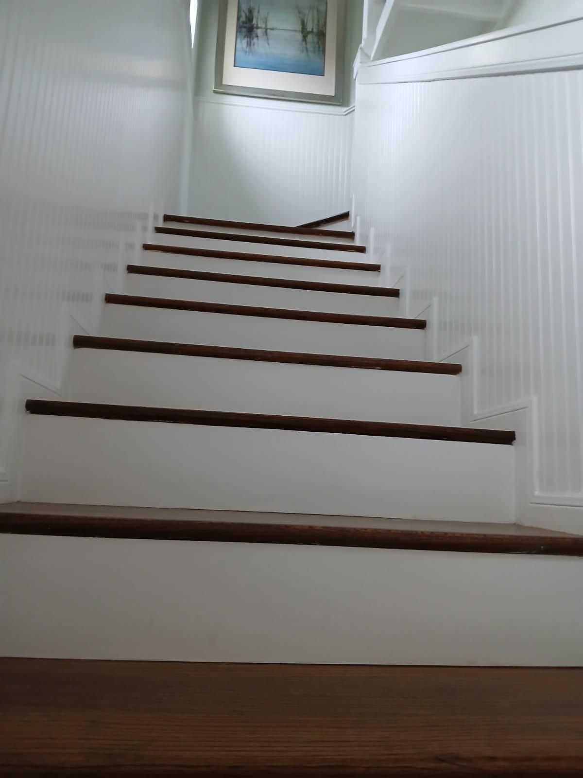 A set of white stairs with wooden steps and a picture on the wall.