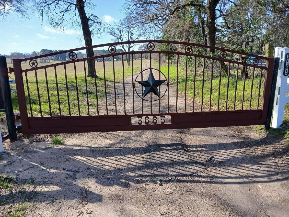 A wrought iron gate with a star on it is open to a dirt road.