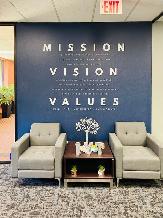 Lobby seating area with blue wall reading “Mission Vision Values” above two armchairs and a small table