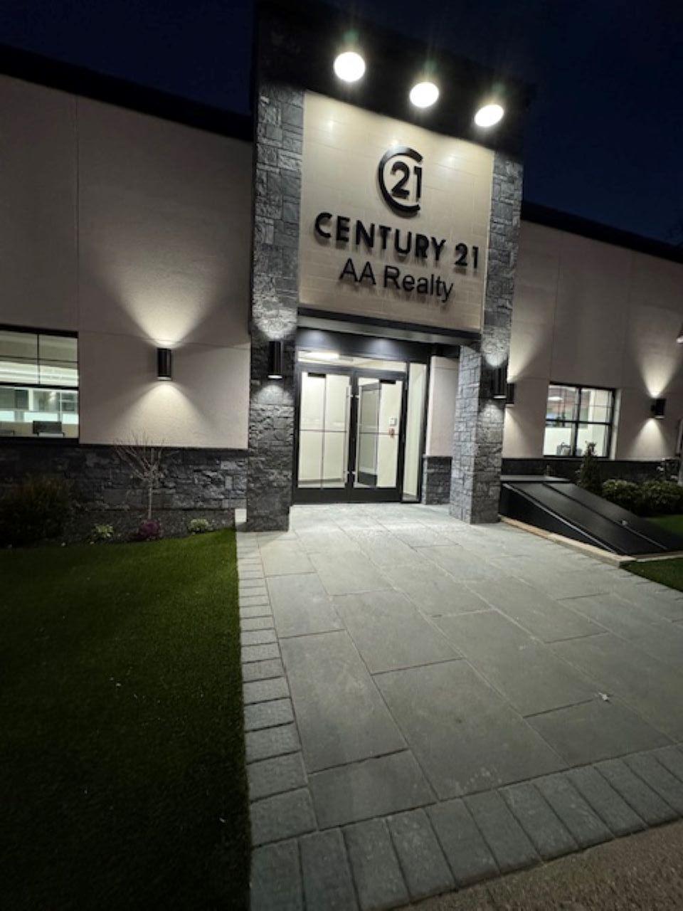 Night view of a Century 21 AA Realty office entrance with lit walkway and stone facade