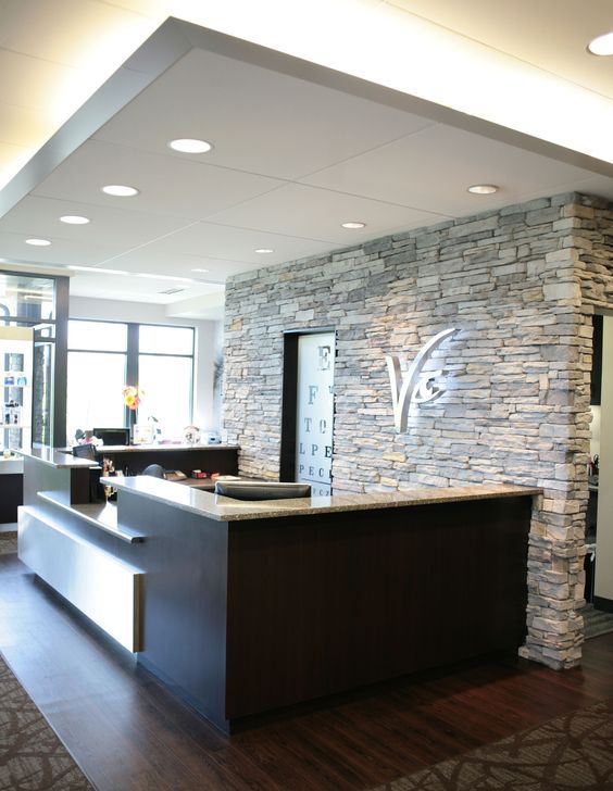 Modern lobby reception desk with dark wood counter and stone accent wall in bright interior.