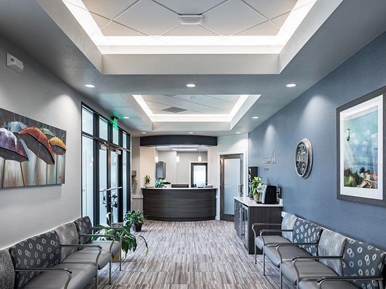 Modern waiting room with gray seating, blue walls, skylights, and a reception desk ahead